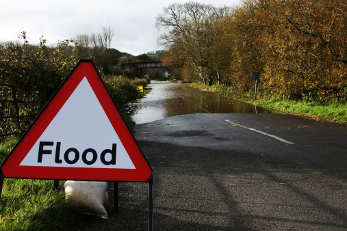 Flood warning sign in foreground with flooded road in background