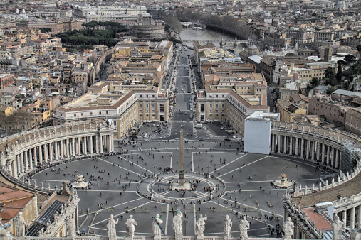 Rome, Italy - April 14, 2015:  Vatican City is the world's smallest independent state in the world and it is surrounded entirely by a brick wall as its boundary.  The Citte del Vaticano sits in the middle of Rome, Italy, measuring 110 acres.  It is home to St. Peter's Basilica, the Sistine Chapel and the Vatican Museums, as well as to the Pope of the Catholic Church.  Pictured here is a statue of St. Peter outside the basilica with all of the saints lining the eaves around St. Peter's Square.
