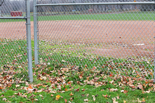 Entrance through the backstop chainlink fence behind home plate on a rural town's municipal softball field in late autumn.