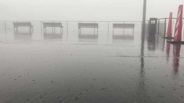 Empty wet parking spaces and sitting wooden benches at river channel waters edge on foggy misty stormy day