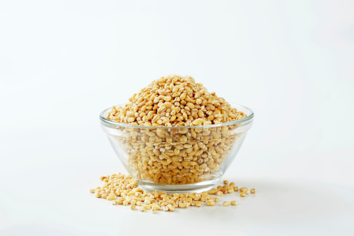 pile of peeled barley in a glass bowl on a white background