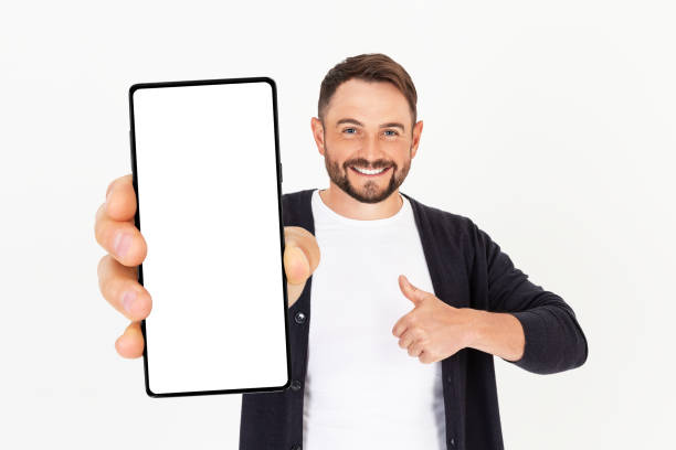 istock Handsome young man holding a smartphone mockup with a blank screen and smiling on a white background. 1749995349