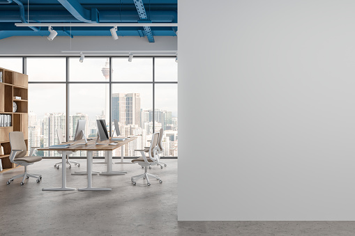 Stylish coworking interior with pc monitors on table in row, shelf with documents and clock. Panoramic window on Kuala Lumpur skyscrapers. Mockup copy space wall partition. 3D rendering