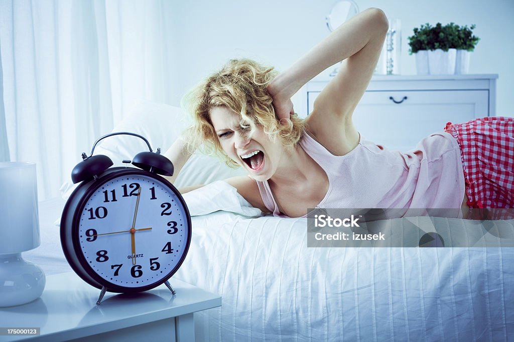 Young woman in a bedroom Young woman lying on her bed in the morning, covering ears with hands and screaming at alarm clock. 25-29 Years Stock Photo