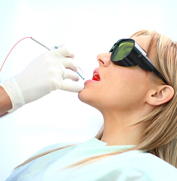 Dental treatment with laser. Closeup of laser dental treatment. Adult female patient is wearing protective glasses while dentist is performing this procedure. Side view. medical laser photos stock pictures, royalty-free photos & images
