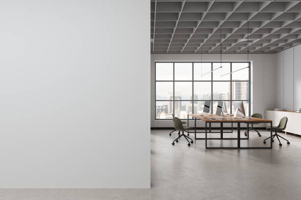 istock White coworking interior with pc monitors and desk near window. Mock up wall 1750005295