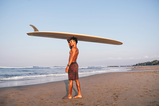 man carrying surfboard and preparing to go surfing at dawn