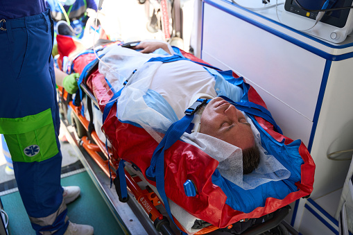 Patient on a stretcher is loaded into an ambulance, experienced paramedics put him on a drip