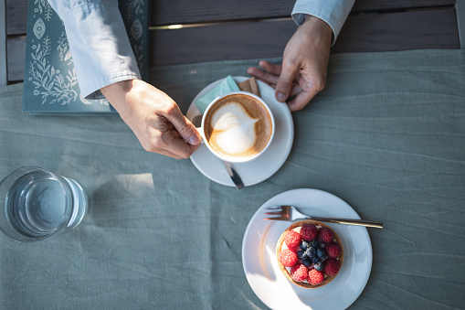 Directly above photo of woman hand holding the coffee cup. On the table is also the sweet dessert