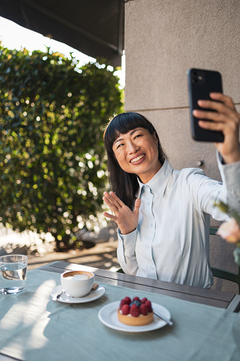 Woman sitting at cafe, enjoying coffee and dessert. She is taking picture with her mobile phone