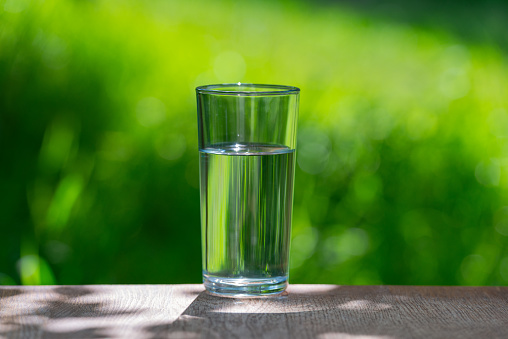 One glass of pure water on a green background of the garden. Water and health.