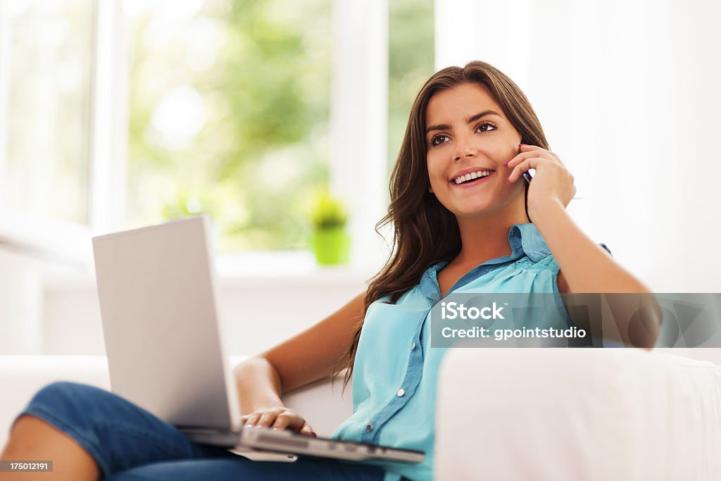 Happy woman paying using laptop and talking on mobile phone Adult Stock Photo