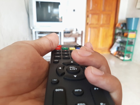 The hand of an unknown person holding the remote control to turn off the tv