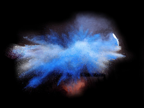Bizarre forms of silver and blue glitter powder paint explode in front of a black background to give off fantastic colors and forms.