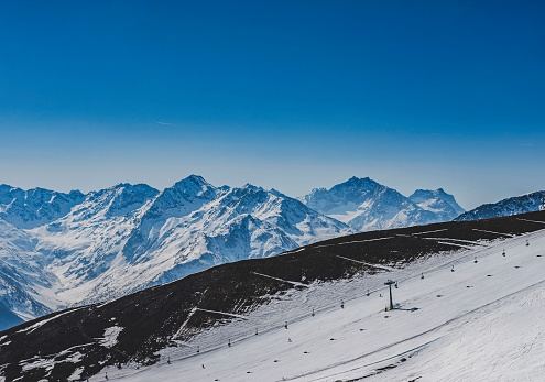 A picturesque vista of Livigno as spring begins to melt the snows of winter. The majestic snow-capped peaks of the Italian Alps loom over a ski slope, signaling the close of the ski season. The image encapsulates the delicate balance of nature’s transition from winter’s chill to spring’s warmth.