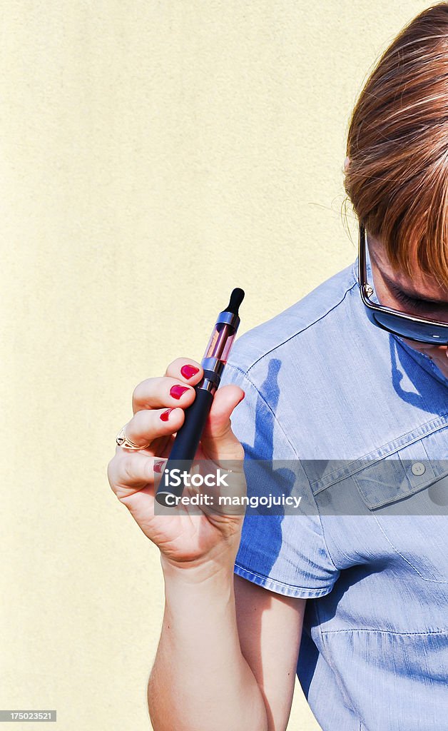 A woman using an e-cigarette half in the image frame Young beautiful redhead using electronic cigarette, safer imitation of normal cigarette Electronic Cigarette Stock Photo