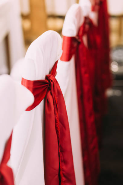 istock Decorative white mantles and red colored ribbons on chairs. Decorated chairs with red bows in a row. Silk bow tied on back of chair in party at restaurant. 1750237831