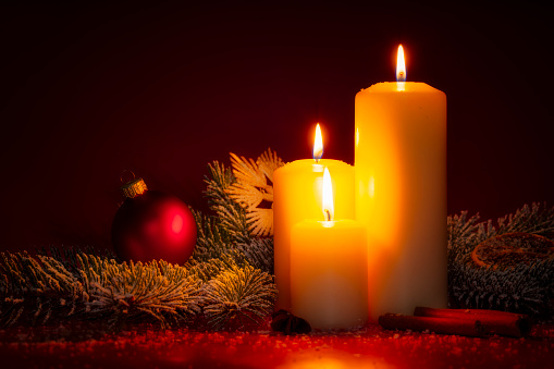Fourth Advent, four candles are lighted, Christmas decoration and gifts on rustic wooden planks against a dark brown background with copy space, selected focus, narrow depth of field