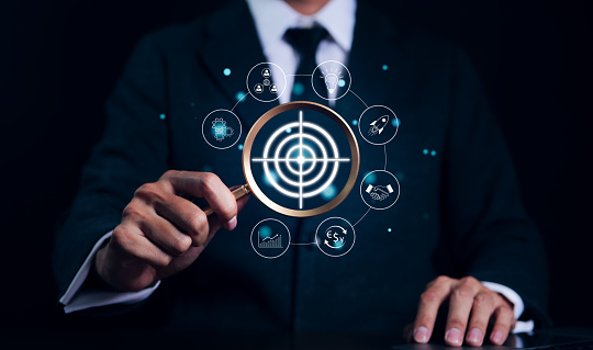 Targeting business and investment concept. Businessman holding a magnifying glass looking target with icons. Digital marketing target planning development, Achieve business goals. Company Vision,