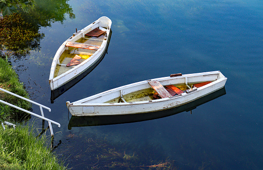 Two old empty wooden boats tied in blue river water