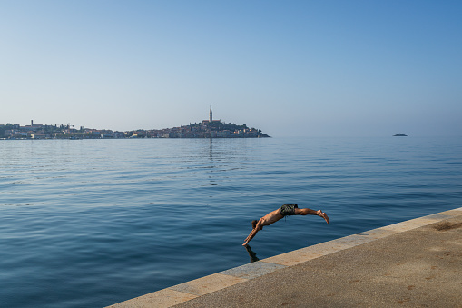 Rovinj, Croatia - October 11, 2023 : A young man jumps into the water. Rovinj is a popular tourist destination on the Adriatic coast in Croatia.