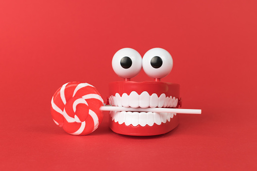 A wind-up toy with teeth and eyes with a lollipop on a red background. The concept of a holiday and parties.