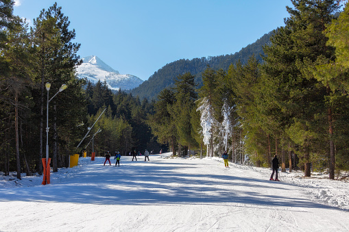 Bansko, Bulgaria - February 11, 2023: Winter landscape with ski road and skiers in famous resort and Todorka peak