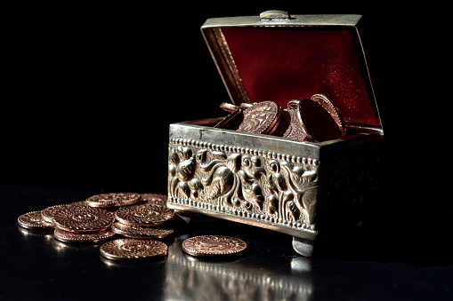 A silver chest full of golden coins on top of a black table