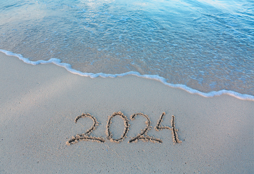 Happy New Year 2024 text on the sea beach. Handwritten inscription 2024 on beautiful white sand beach