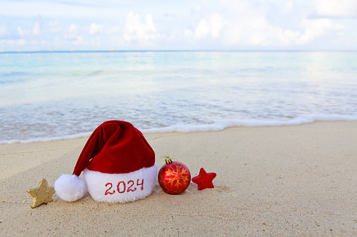 Merry Christmas hat and Decorations on the white Caribbean Sand. New Year 2024 background