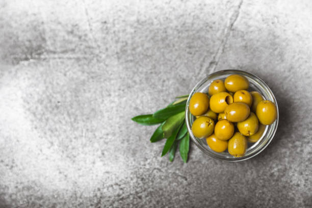 istock Tasty black olives  on background. Olive and olive tree branches on a white table. Delicacy. 1750440073