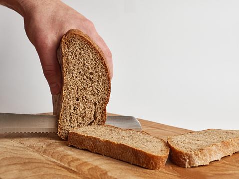 Cut bread on a wooden board with a knife. Work in the kitchen.