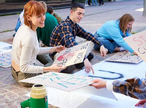 Group of teenager students sitting on street and making placards for protest against climate change and to save planet