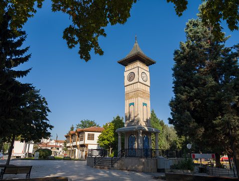 Clock Tower of Tirana against the blue sky in Albania. Square chapel in Islamic style among greenery, close-up