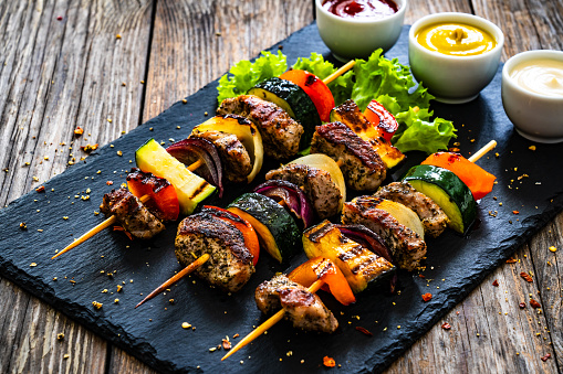 Shashlik - grilled meat and vegetables on stone plate on black wooden table