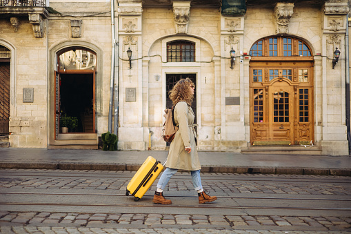 A beautiful and cheerful woman is captured as she walks along a charming, ancient European street during the autumn season