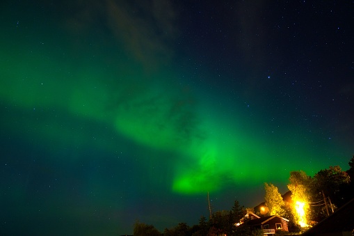 This stunning image displays the majestic aurora borealis illuminating two houses in the night sky