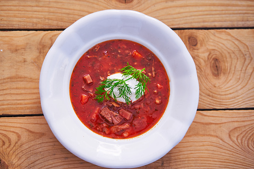 Top view on the rustic style white porcelain deep plate with ukrainian borsch soup. Traditional, delicious and satisfying dish served often like main course for lunch in the eastern european cuisine.