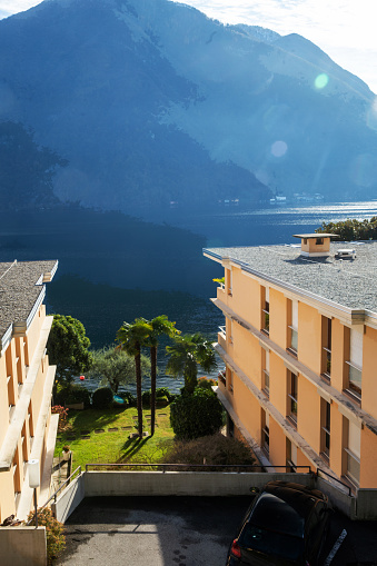 Gap between houses on the shore of Lugano lake with amazing garden there . Suburb of Lugano city. There are pebbles on the roof. Swiss Alps on other side of lake