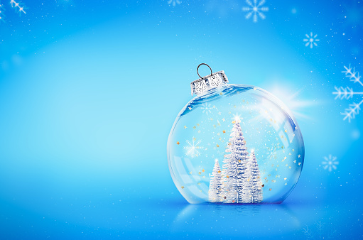 transparent Christmas ball with silver Christmas trees inside on a blue background. The place for