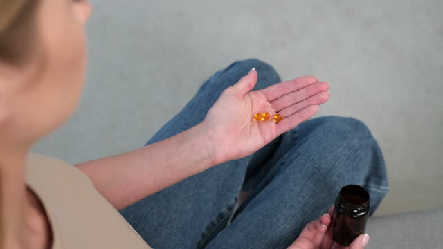 The woman takes omega pills into her palm.