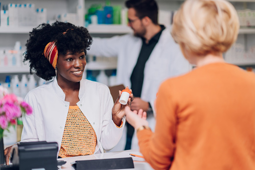 Young african american woman pharmacist and senior customer talking about medication in pharmacy. Black female health care worker with an afro hair working in a drugstore. Copy space.