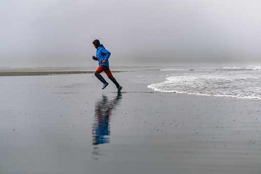 A sportsman is jogging in nature next to the ocean and running from the waves. A runner is exercising in nature on the beach in Iceland.