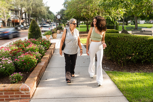 This is a candid photograph of a senior Puerto Rican woman in her 70s walking and talking with her adult granddaughter in Winter Park, Florida on a sunny day.