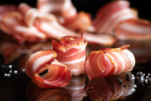 Bacon rolls with fresh spices on a black glass background