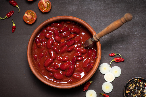 Red Mexican beans in a ceramic bowl on a rustic black-gray background, chili peppers and cherry tomatoes around