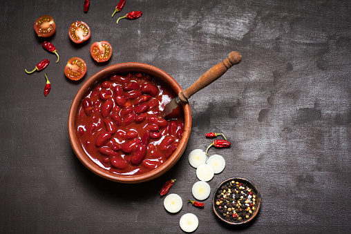 Red Mexican beans in a ceramic bowl on a rustic black-gray background, chili peppers and cherry tomatoes around