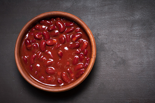 Red Mexican beans in a ceramic bowl on a rustic black-gray background with copy space