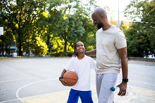 Portrait of a Latin American man and his son having fun playing basketball at the outdoor basketball court.