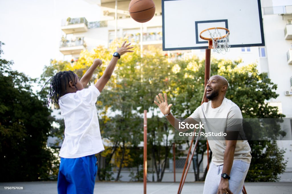 Boy Taking A Shot While Playing Basketball With Father Stock Photo